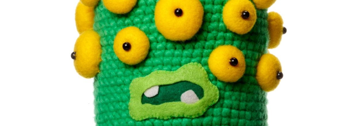 Detail of a crocheted monster head with several yellow eyes and an open mouth with two teeth