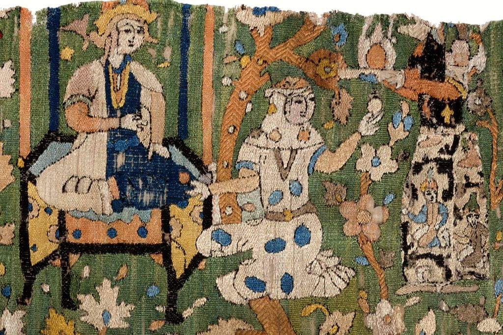 Detail of a textile with a woman seated on a cushion on the left, an attendant at the center turning to the right, and a man on the far right carrying a pitcher