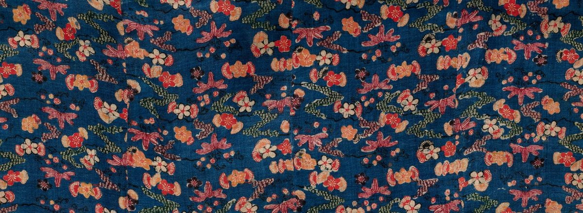 Detail of a textile with a dark blue background covered in a floral pattern with orange, red and white flowers