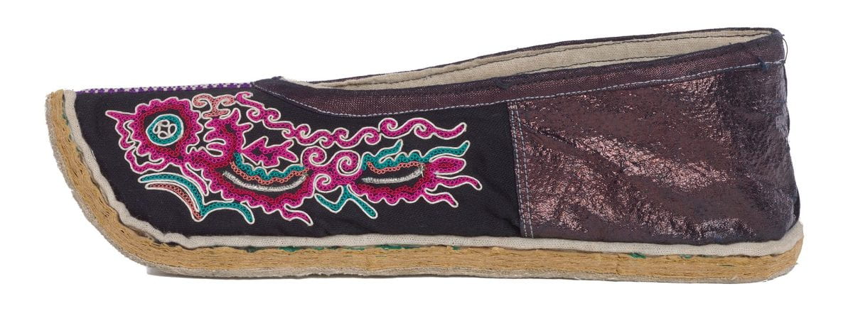 Side view of a pointed, flat shoe with bright embroidery covering the top, front portion of the shoe