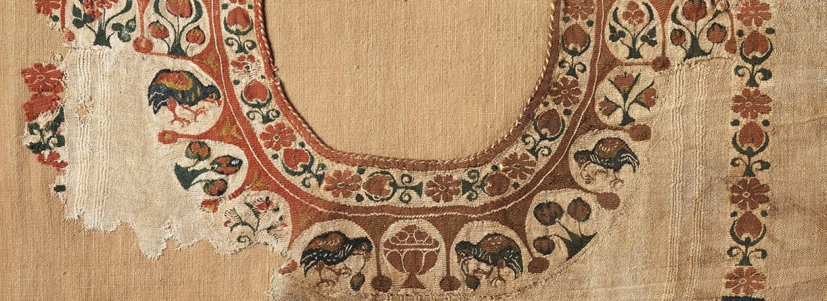 Linen tunic fragment decorated with red fruit, flowers, and birds in arches.