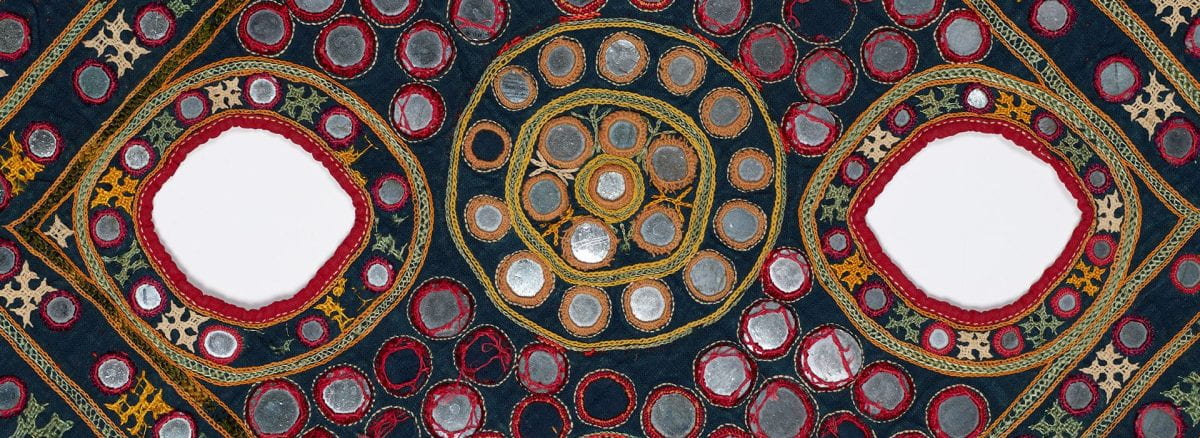 Detail of a colorful textile covered in small, circular mirrors and embroidery with two small holes next to one another