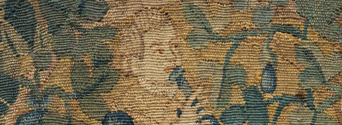 Detail of a tapestry featuring a boy holding an instrument to his mouth surrounded by foliage