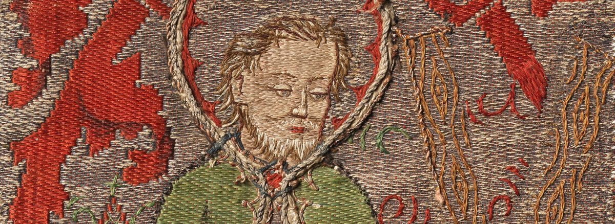 A fragment of woven silk and metallic-wrapped yarn with embroidery depicting Saint Andrew the Apostle wearing a green robe surrounded by red and silver vines and foliage.
