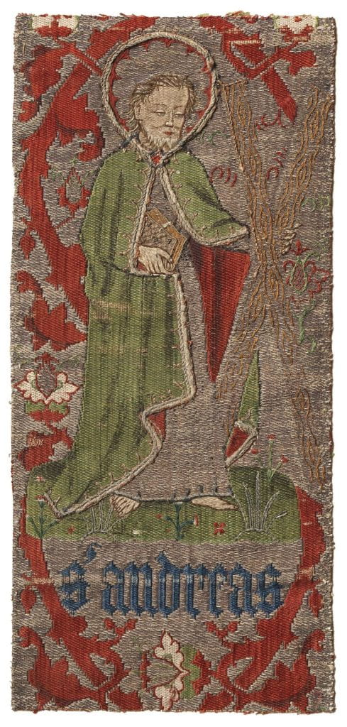 A fragment of compound-woven silk and metallic-wrapped yarn embroidery depicting Saint Andrew the Apostle wearing a green robe surrounded by red and silver vines and foliage. He stands barefoot over "S' Andreas" written in blue Gothic letters.
